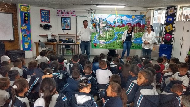 Tres profesores en un salón dando explicaciones y clases a los muchos niños que se encuentran sentados enfrente de ellos