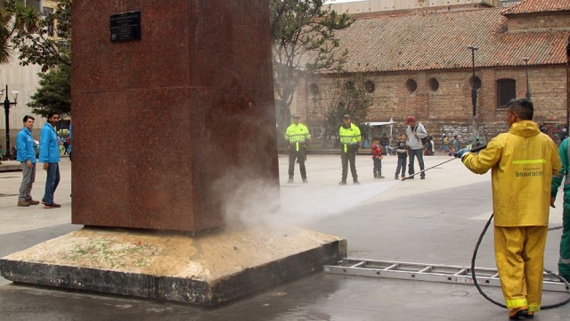 Un trabajador de la uaesp rociando agua con una manguera a un poste sucio del centro de Bogotá
