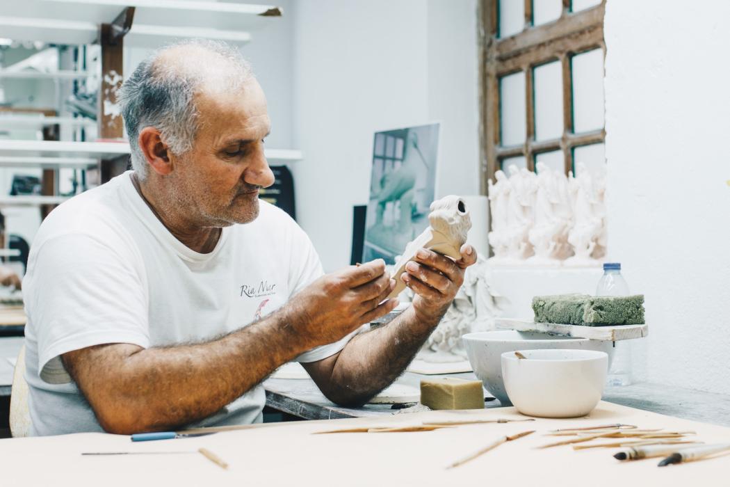 Un adulto mayor pintando un muñeco en cerámica 