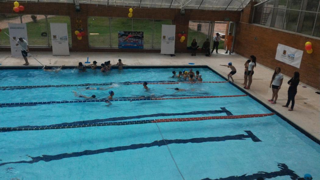 Plano general de una piscina, hay varios niños entrenando en la piscina con sus profesoras afuera guiándolos en Ciudad Bolívar