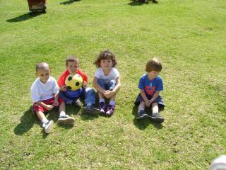 Grupo de cuatro niños pequeños sentados sobre el pasto.