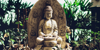 Una estatua mediana de un buda meditando en un pequeño jardín.