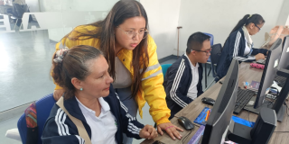 Imagen de una funcionaria ayudándole a una señora en un computador