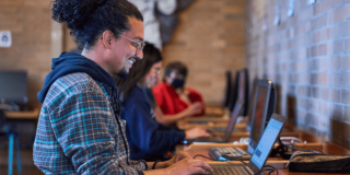 Imagen de un hombre sonriendo al frente de un computador portátil