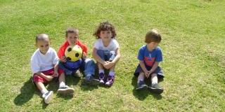 Grupo de cuatro niños pequeños sentados sobre el pasto.