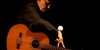 Imagen del titíritero sentado con una guitarra en sus piernas
