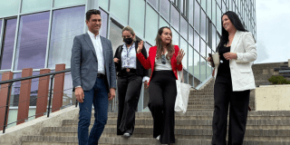 Foto de un grupo de cuatro personas que desciende unas escaleras frente a un edificio moderno mientras conversan y sonríen.