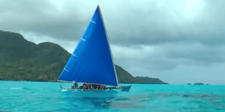 Imagen de un velero que navega en un gran mar azul, al fondo se ven algunas montañas